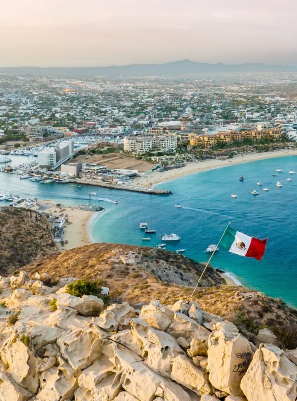 Vibrant flag waving in the foreground of a picturesque cityscape. Cabo San Lucas, Mexico.